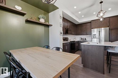 This kitchen features dark wood cabinetry, stainless steel appliances, and a kitchen island with a sink and seating - 405 Genesis Court, Stony Plain, AB - Indoor