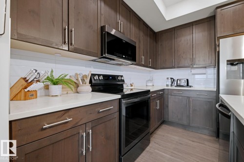 The kitchen features dark wood cabinetry, white countertops, and a white subway tile backsplash - 405 Genesis Court, Stony Plain, AB - Indoor Photo Showing Kitchen With Upgraded Kitchen