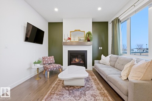 Spacious living area featuring hardwood flooring, a fireplace with a mantel, and large windows providing ample natural light - 405 Genesis Court, Stony Plain, AB - Indoor Photo Showing Living Room With Fireplace