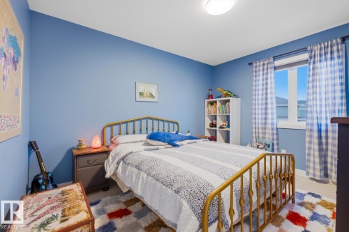 This room features light blue walls, a window with plaid curtains, and a ceiling light fixture - 405 Genesis Court, Stony Plain, AB - Indoor Photo Showing Bedroom