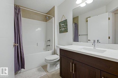 The bathroom features a white bathtub with a shower, a dark wood vanity with a white countertop and an integrated sink, and a large mirror - 405 Genesis Court, Stony Plain, AB - Indoor Photo Showing Bathroom