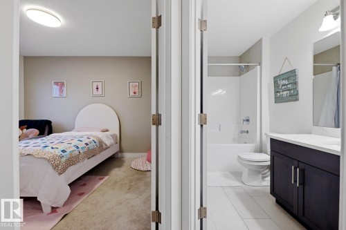 The property features a bedroom with neutral wall tones and a ceiling light fixture, alongside a bathroom with a white vanity top, a dark vanity cabinet with silver handles, a mirror, and a bathtub with a shower - 405 Genesis Court, Stony Plain, AB - Indoor Photo Showing Bathroom