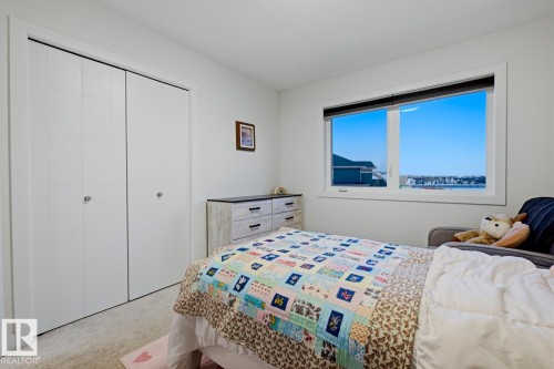 This room features light-colored carpeting, a window with a view, and a closet with bifold doors - 405 Genesis Court, Stony Plain, AB - Indoor Photo Showing Bedroom