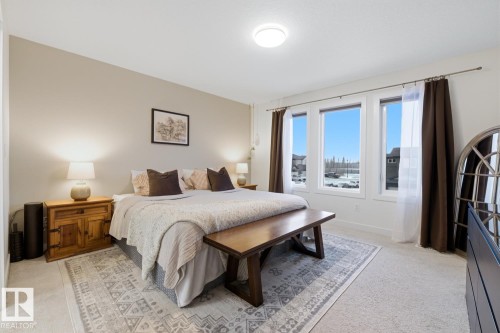 This bedroom features light-colored carpeting, three large windows, and a ceiling light fixture - 405 Genesis Court, Stony Plain, AB - Indoor Photo Showing Bedroom