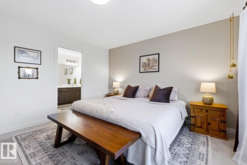 Bedroom with light-colored walls and carpeted flooring, featuring a large bed with dark pillows, and an area rug - 405 Genesis Court, Stony Plain, AB - Indoor Photo Showing Bedroom
