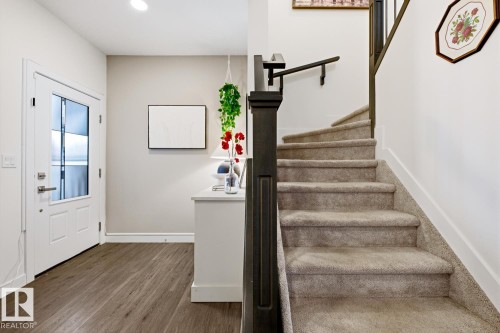 Entryway featuring wood style flooring, a white front door with glass panels, and a carpeted staircase with a dark baluster and handrail - 405 Genesis Court, Stony Plain, AB - Indoor Photo Showing Other Room