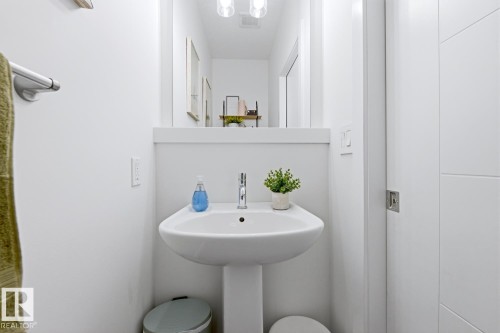 The bathroom features a pedestal sink with a chrome faucet, a white vanity mirror, and recessed lighting - 405 Genesis Court, Stony Plain, AB - Indoor Photo Showing Bathroom