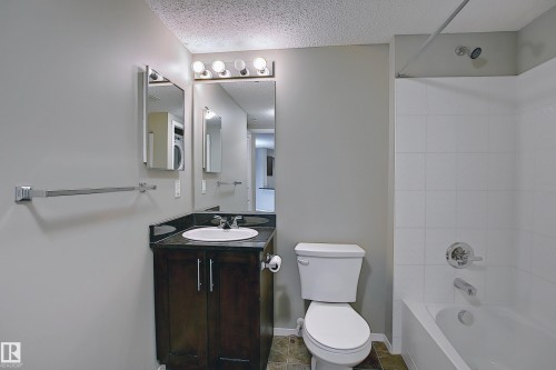 Bathroom featuring a vanity with dark wood-finish cabinetry, a dark countertop, and an undermount sink - 114 3207 James Mowatt Trail, Edmonton, AB - Indoor Photo Showing Bathroom