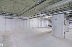 Concrete parking space featuring exposed concrete walls and ceiling, overhead piping, and fluorescent lighting - 
