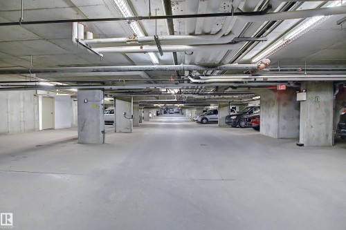 Spacious underground parking garage featuring concrete walls and flooring, overhead utility piping, and fluorescent lighting - 114 3207 James Mowatt Trail, Edmonton, AB - Indoor Photo Showing Garage