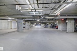 Spacious underground parking garage featuring concrete walls and flooring, overhead utility piping, and fluorescent lighting - 