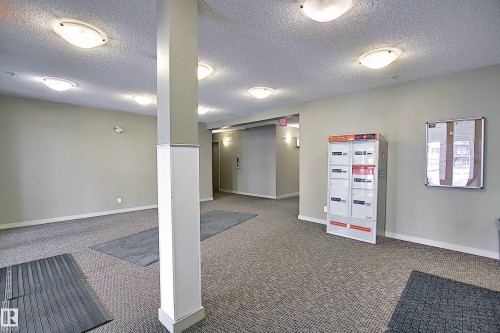 Building common area featuring wall-to-wall carpeting, multiple flush-mount ceiling lights, and a central structural column - 114 3207 James Mowatt Trail, Edmonton, AB - Indoor