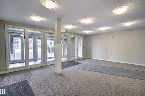 Spacious common area featuring textured carpet flooring, neutral painted walls, and multiple flush-mount ceiling lights - 114 3207 James Mowatt Trail, Edmonton, AB - Indoor Photo Showing Other Room