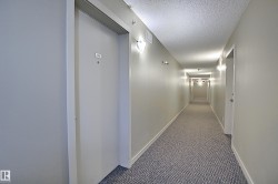 Long corridor featuring wall-mounted lighting fixtures, textured ceiling, and patterned carpet flooring - 