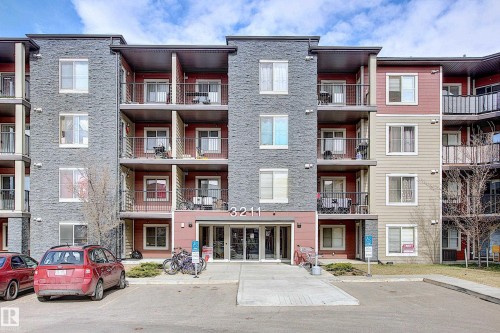 Multi-story building with a stone facade, red and beige siding, multiple balconies with metal railings, and a central glass entrance - 114 3207 James Mowatt Trail, Edmonton, AB - Outdoor With Facade
