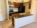 Kitchen with dark wood cabinetry, stainless steel oven and microwave, black refrigerator, and dark granite countertops - 114 3207 James Mowatt Trail, Edmonton, AB  - Indoor Photo Showing Kitchen With Double Sink 