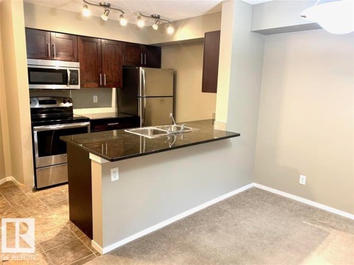 Kitchen featuring dark wood cabinetry, stainless steel appliances, and track lighting - 114 3207 James Mowatt Trail, Edmonton, AB - Indoor Photo Showing Kitchen With Stainless Steel Kitchen With Double Sink