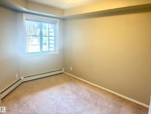 Room featuring an expansive window with bright natural illumination, neutral wall color, baseboard trim, and a built-in heating unit - 114 3207 James Mowatt Trail, Edmonton, AB - Indoor Photo Showing Other Room