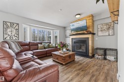 Living area featuring a wood-finish flooring, a prominent fireplace with a wood-paneled surround and mantel, and a bay window - 