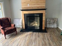 Fireplace featuring a natural wood-finish surround and mantel, black tile hearth, and a glass-front insert - 