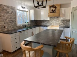 Kitchen featuring white cabinetry with dark hardware, dark stone-finish countertops, and a gray brick-patterned backsplash - 