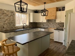 Kitchen featuring a central island with dark counters, white shaker-style cabinetry, and a stone-finish backsplash - 