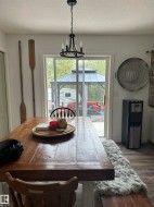 Dining area featuring a rustic wood-finish table, a contemporary black chandelier, and sliding glass doors opening to a covered outdoor structure - 