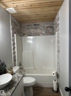 Bathroom featuring a wood-finish plank ceiling, a white shower/tub combination, and stacked stone-effect tile surrounding the shower - 