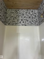 Shower enclosure featuring white and grey pebble tile surround and a wood-finish ceiling - 