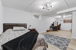 Open-concept room featuring light-toned wood-finish flooring, a drop ceiling, and modern multi-bulb light fixtures - 