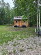 Rustic wood-sided outbuilding featuring a pitched roof, two windows, and a wooden entrance door with a small porch - 