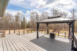 Expansive outdoor deck featuring a gazebo with a solid roof, wood plank flooring, and a perimeter railing, surrounded by natural woodland - 