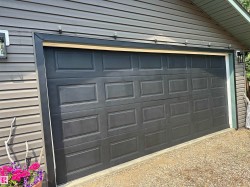 Garage featuring a paneled door, dark siding, and exterior lighting - 
