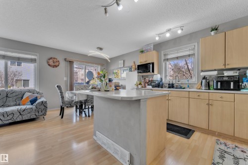 Open-concept kitchen featuring light wood-finish cabinetry, a large kitchen island with a light-toned countertop, and light wood-finish flooring - 64 4350 23 Street, Edmonton, AB - Indoor Photo Showing Kitchen