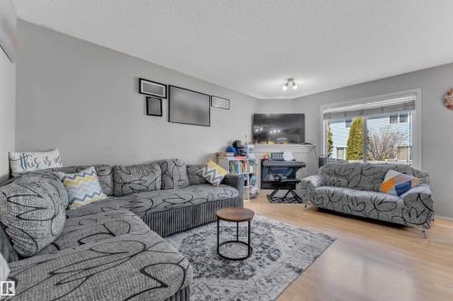Living area featuring light wood-finish flooring, a large window with horizontal blinds, and neutral wall tones - 64 4350 23 Street, Edmonton, AB - Indoor Photo Showing Living Room With Fireplace