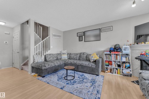 Living area with light wood-finish flooring, a staircase with white railings, and painted walls - 64 4350 23 Street, Edmonton, AB - Indoor Photo Showing Living Room