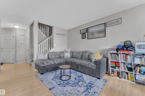 Living area with light wood-finish flooring, a contemporary ceiling light fixture, and a white staircase with matching railing - 64 4350 23 Street, Edmonton, AB - Indoor Photo Showing Living Room