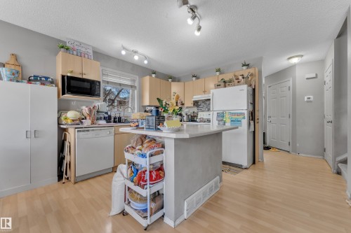Kitchen featuring light wood-finish flooring, light wood cabinetry, a built-in microwave, white appliances, and track lighting - 64 4350 23 Street, Edmonton, AB - Indoor Photo Showing Kitchen