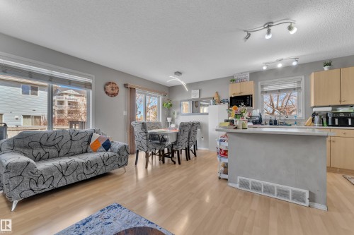 Open-concept living space featuring light wood-finish flooring, a kitchen island with seating, natural wood cabinetry, and large windows - 64 4350 23 Street, Edmonton, AB - Indoor