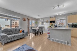 Open-concept living space featuring light wood-finish flooring, a kitchen island with seating, natural wood cabinetry, and large windows - 