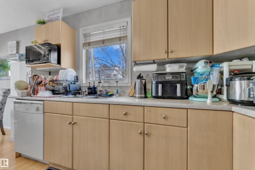 Kitchen featuring extensive wood-finish cabinetry, light-toned countertops, and a built-in dishwasher - 64 4350 23 Street, Edmonton, AB - Indoor Photo Showing Kitchen