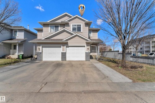 Two-story residence featuring light-toned siding, a dual garage, and a concrete driveway - 64 4350 23 Street, Edmonton, AB - Outdoor With Facade