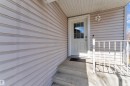Entryway featuring a white paneled door with upper glass inserts, light-colored vinyl siding, a concrete stoop with two steps, a white metal railing, and an exterior wall light fixture - 64 4350 23 Street, Edmonton, AB  - Outdoor With Exterior 
