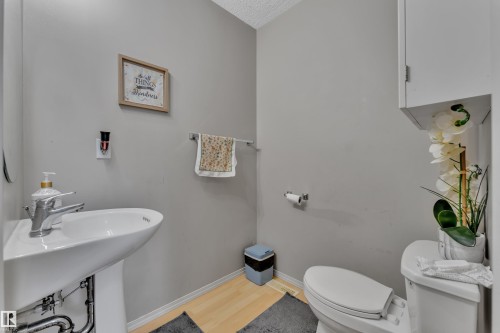 Powder room with a pedestal sink, white toilet, light wood-finish flooring, and light gray wall paint - 64 4350 23 Street, Edmonton, AB - Indoor Photo Showing Bathroom