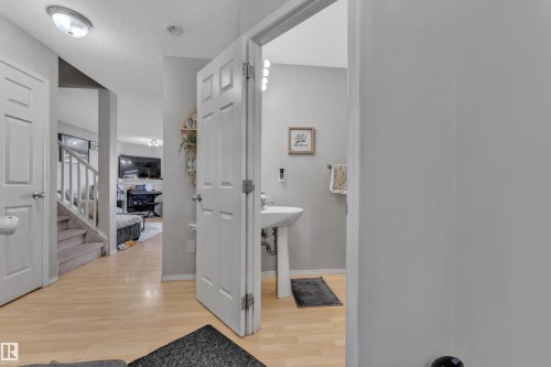 Pedestal sink and wall-mounted vanity lighting visible through an open doorway - 64 4350 23 Street, Edmonton, AB - Indoor Photo Showing Other Room