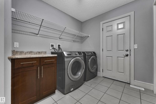 Laundry room featuring tile flooring, built-in cabinetry with a stone-finish countertop, and wall-mounted shelving - 3363 13 Avenue, Edmonton, AB - Indoor Photo Showing Laundry Room