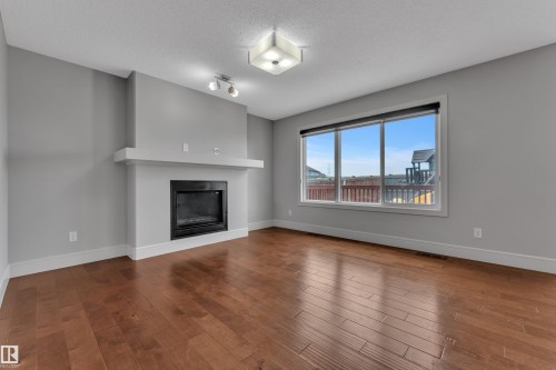 Spacious room featuring wood-finish flooring, a contemporary fireplace with a white mantel, and a large window with white trim - 3363 13 Avenue, Edmonton, AB - Indoor Photo Showing Living Room With Fireplace