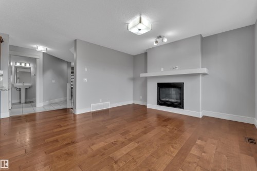 Spacious living area featuring rich wood-finish flooring, a contemporary fireplace with a white mantel, and recessed lighting fixtures - 3363 13 Avenue, Edmonton, AB - Indoor Photo Showing Living Room With Fireplace