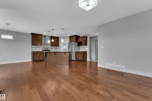 Kitchen featuring rich wood cabinetry, stainless steel appliances, a center island with pendant lighting, and a decorative tile backsplash - 3363 13 Avenue, Edmonton, AB - Indoor Photo Showing Kitchen