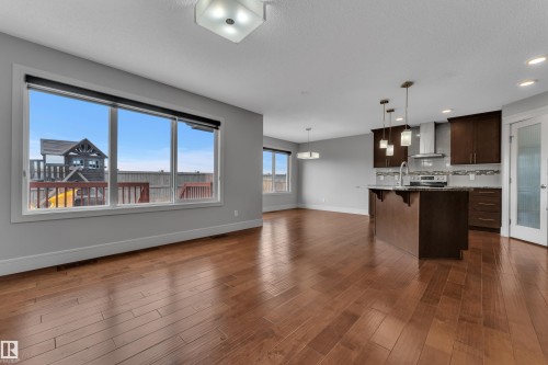 Open concept living space featuring wood-finish flooring, a kitchen island with pendant lighting, dark wood cabinetry, and a stainless steel appliance suite - 3363 13 Avenue, Edmonton, AB - Indoor